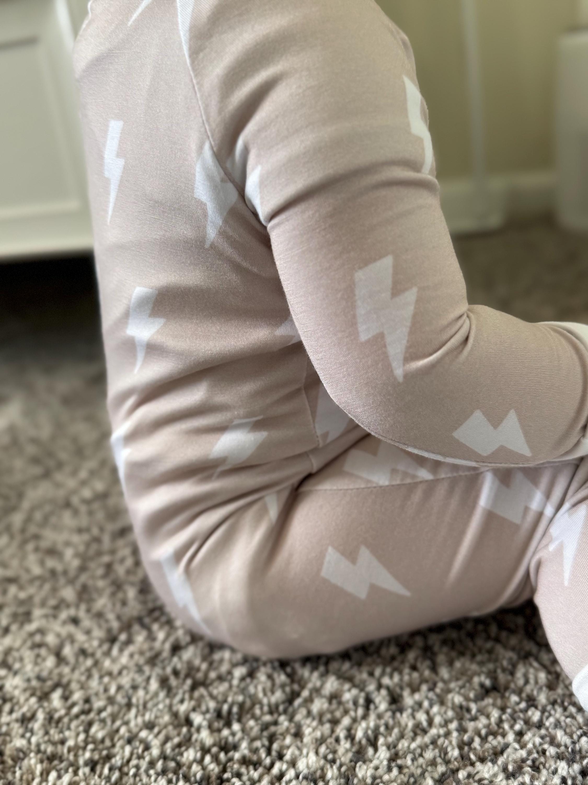 Child wearing rock and roll beige convertible baby pajama with white patterns on a carpeted floor.