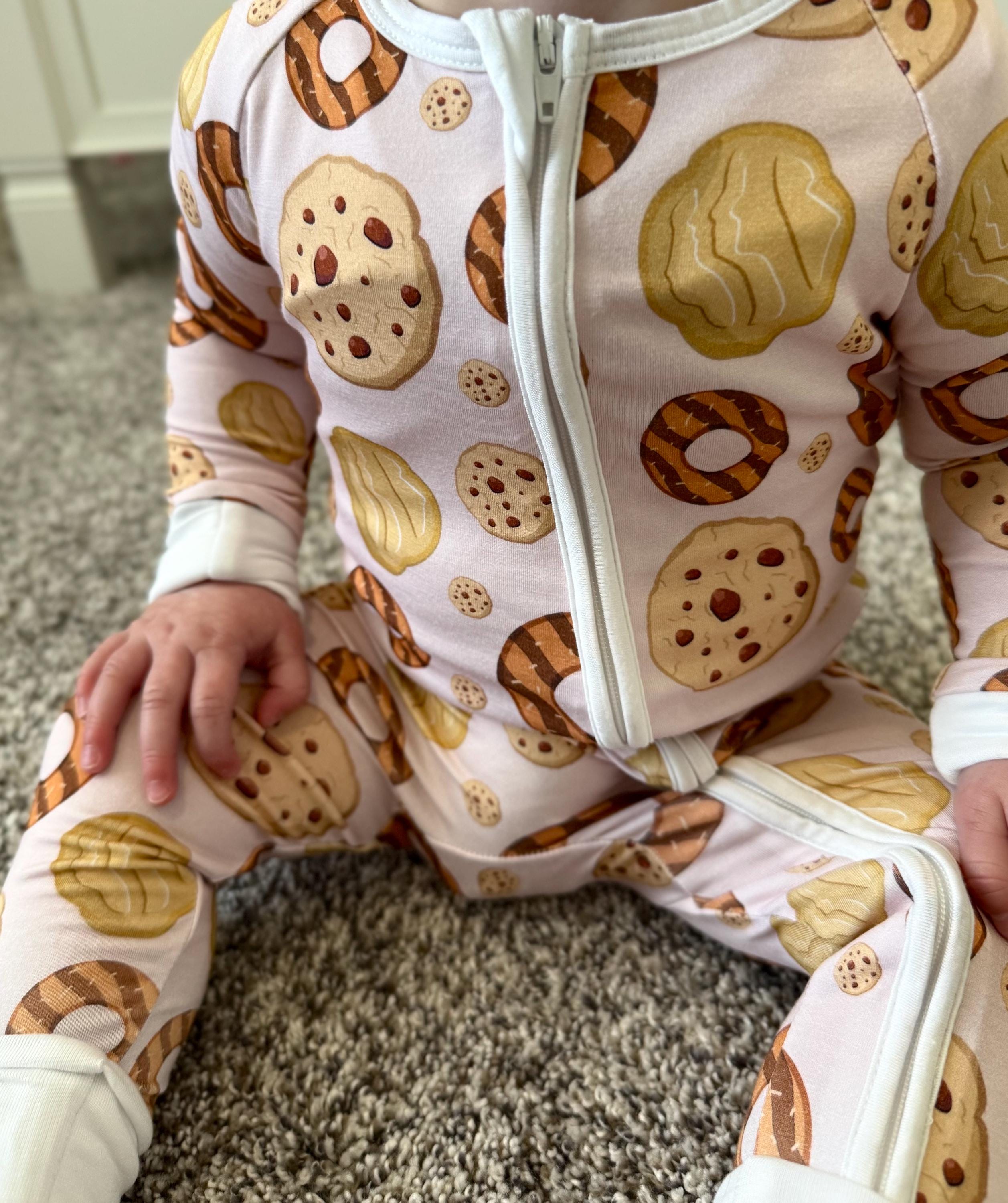 Baby in a bamboo pink convertible footie pjs with cookie pattern sitting on a carpeted floor.
