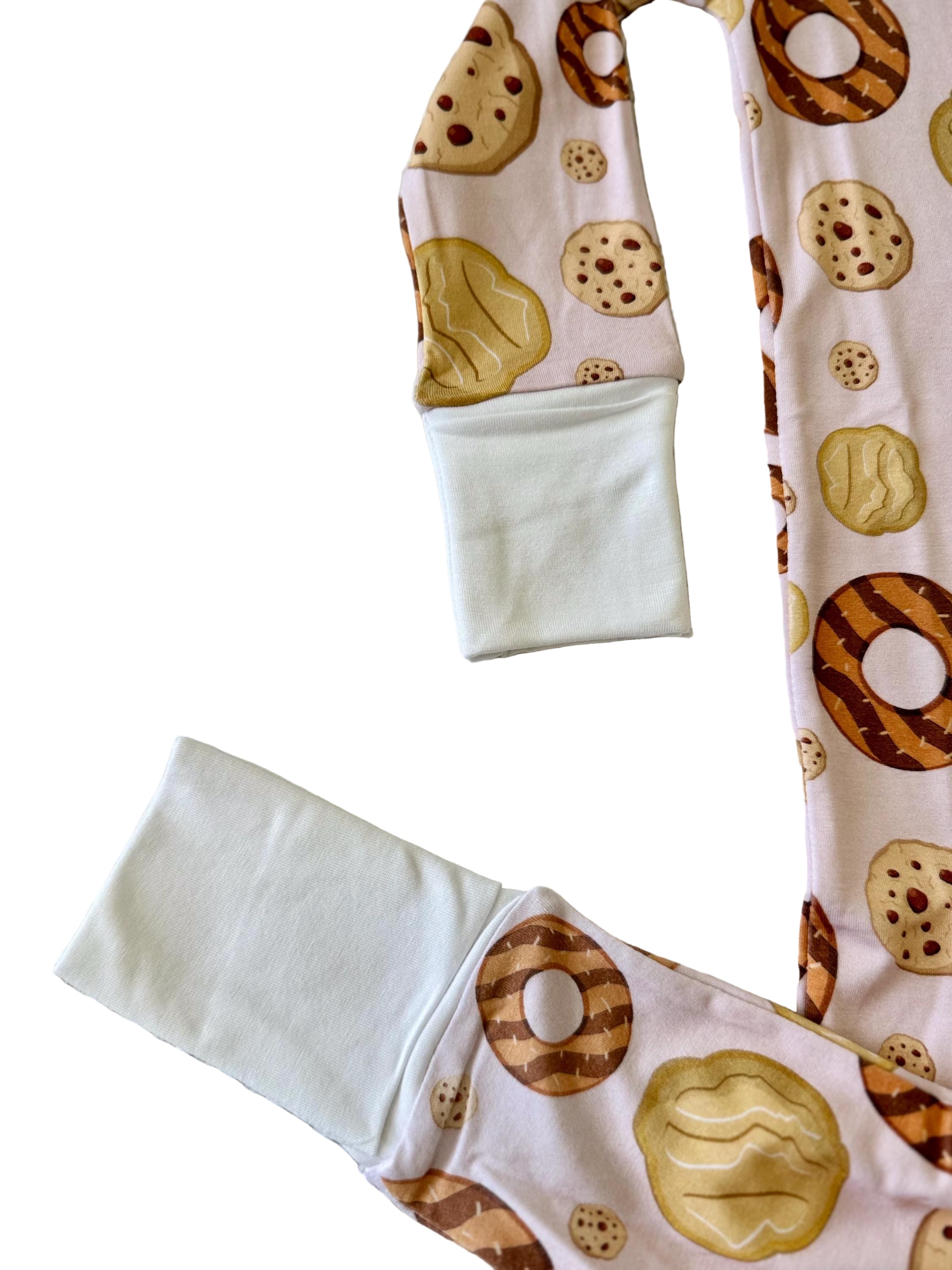 Baby zip up footed pajamas with light pink background with brown and cream girl scout cookie pattern on a textured surface with convertible feet and mittens. 