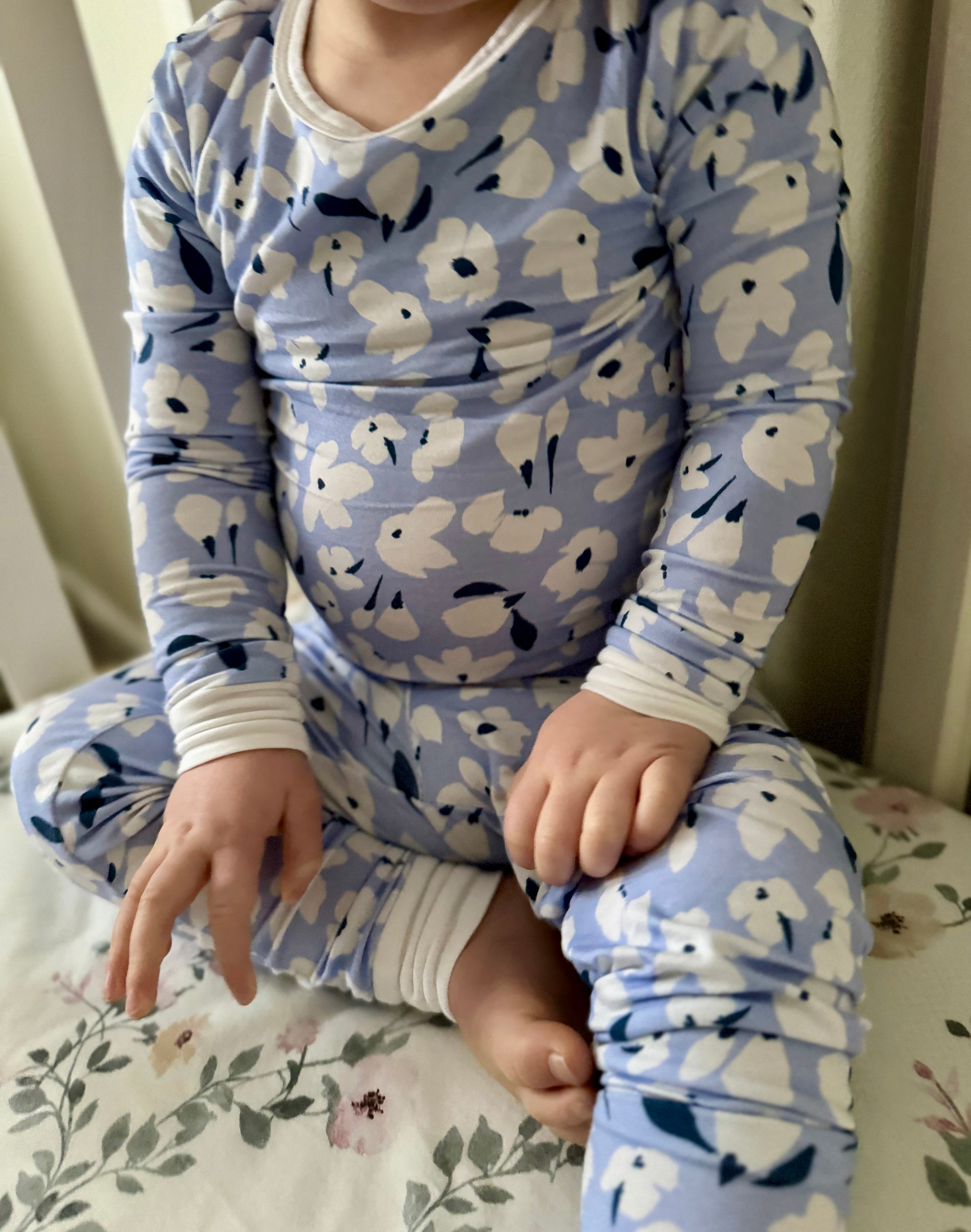 Child wearing blue floral pajamas sitting on a floral bedspread.