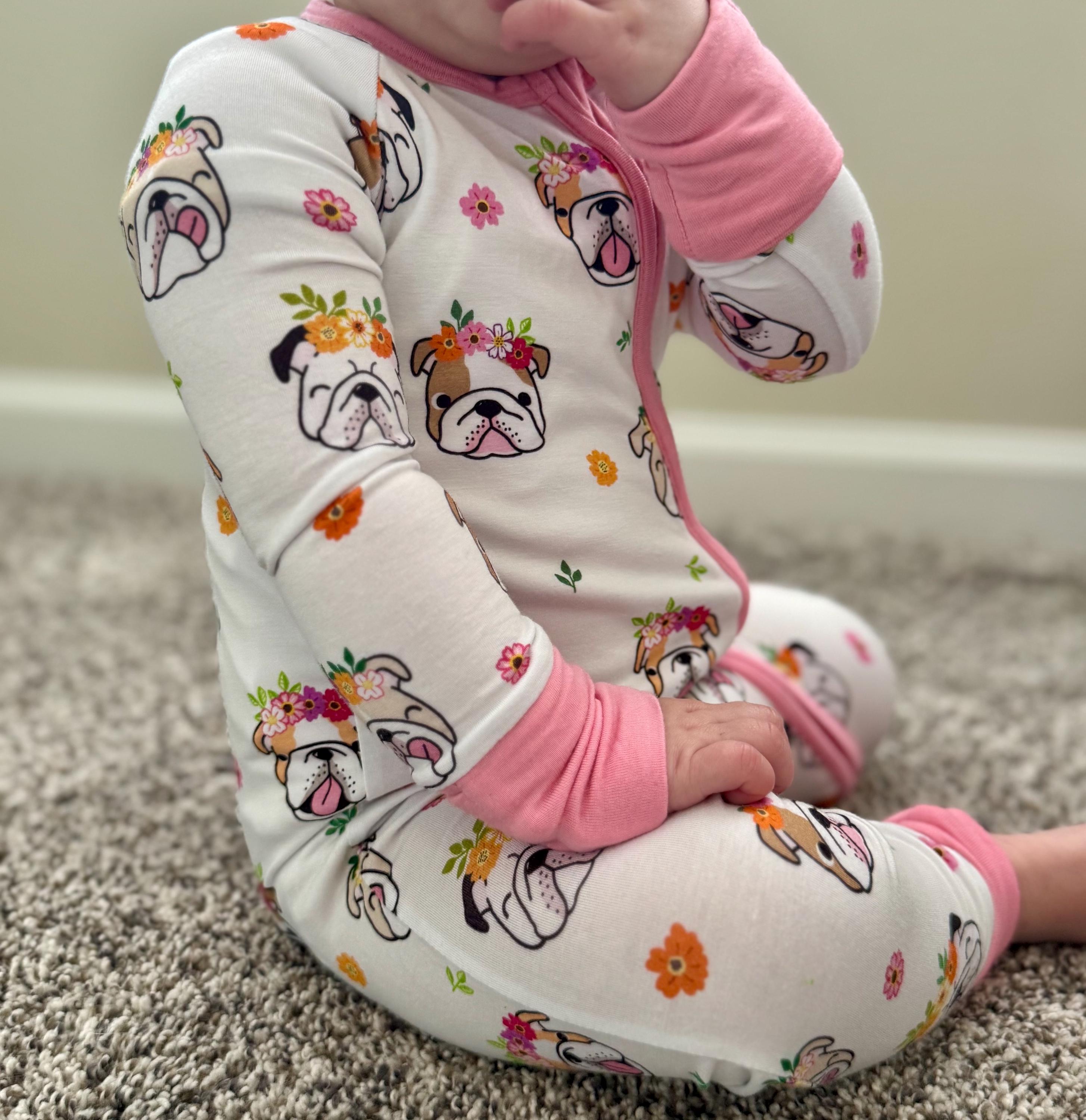 Baby in white bamboo convertible footie pajamas with bulldog puppy faces with flower design and pink zipper, cuffs and footies. 