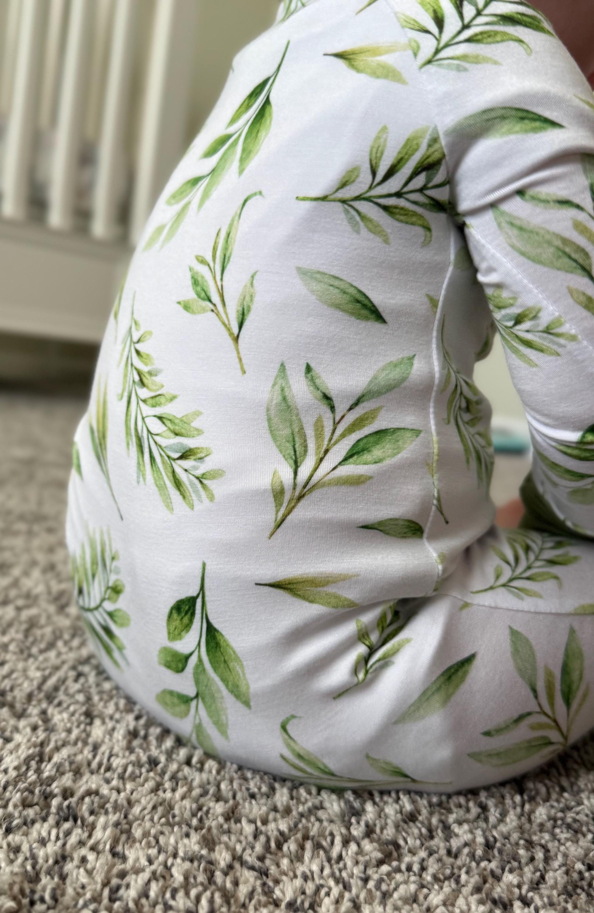 White soft baby convertible pajama with green leaf pattern on a carpeted floor for fall season