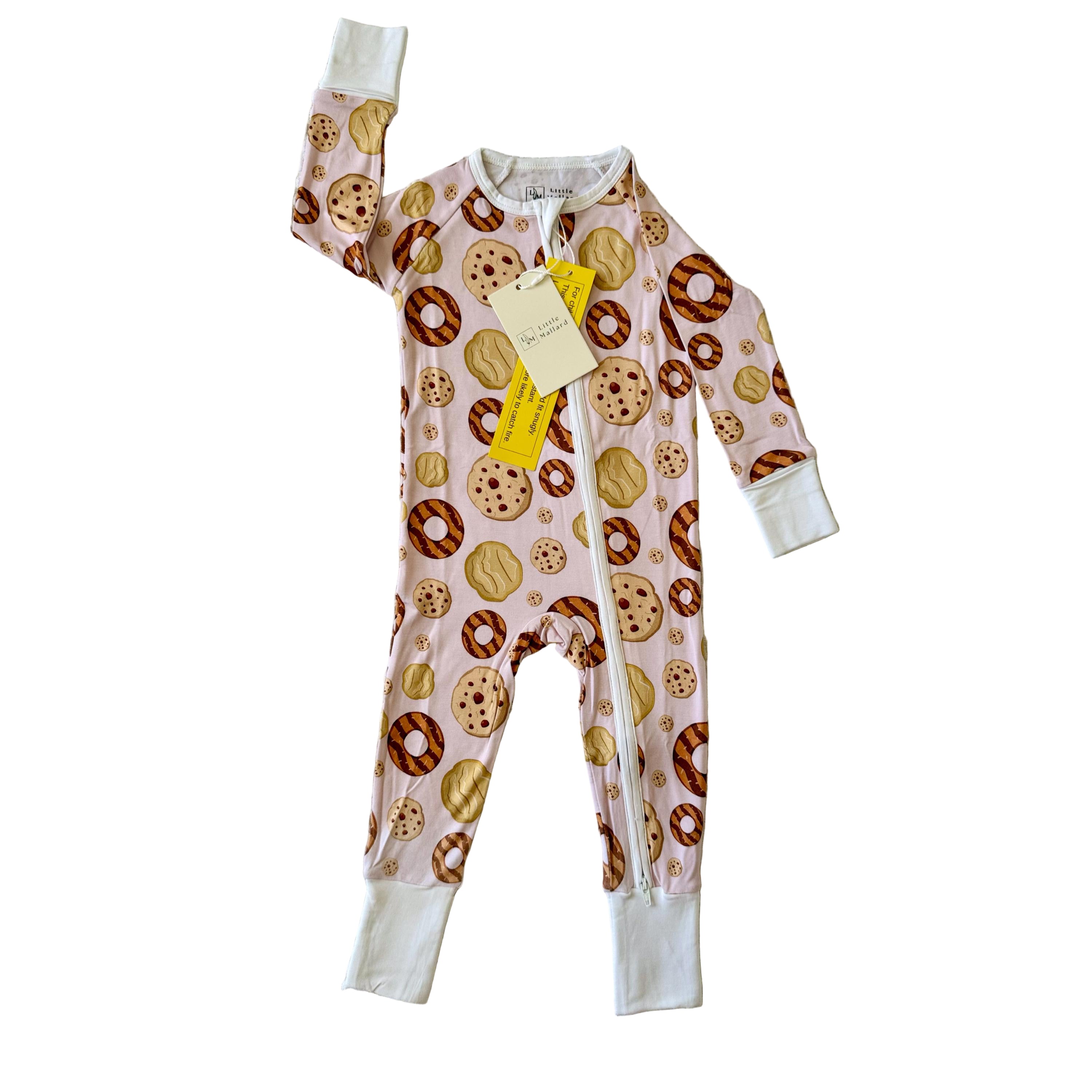 Soft and breathable Pink Children's footie pajama with tan, brown and cream color cookie pattern on a white surface. 