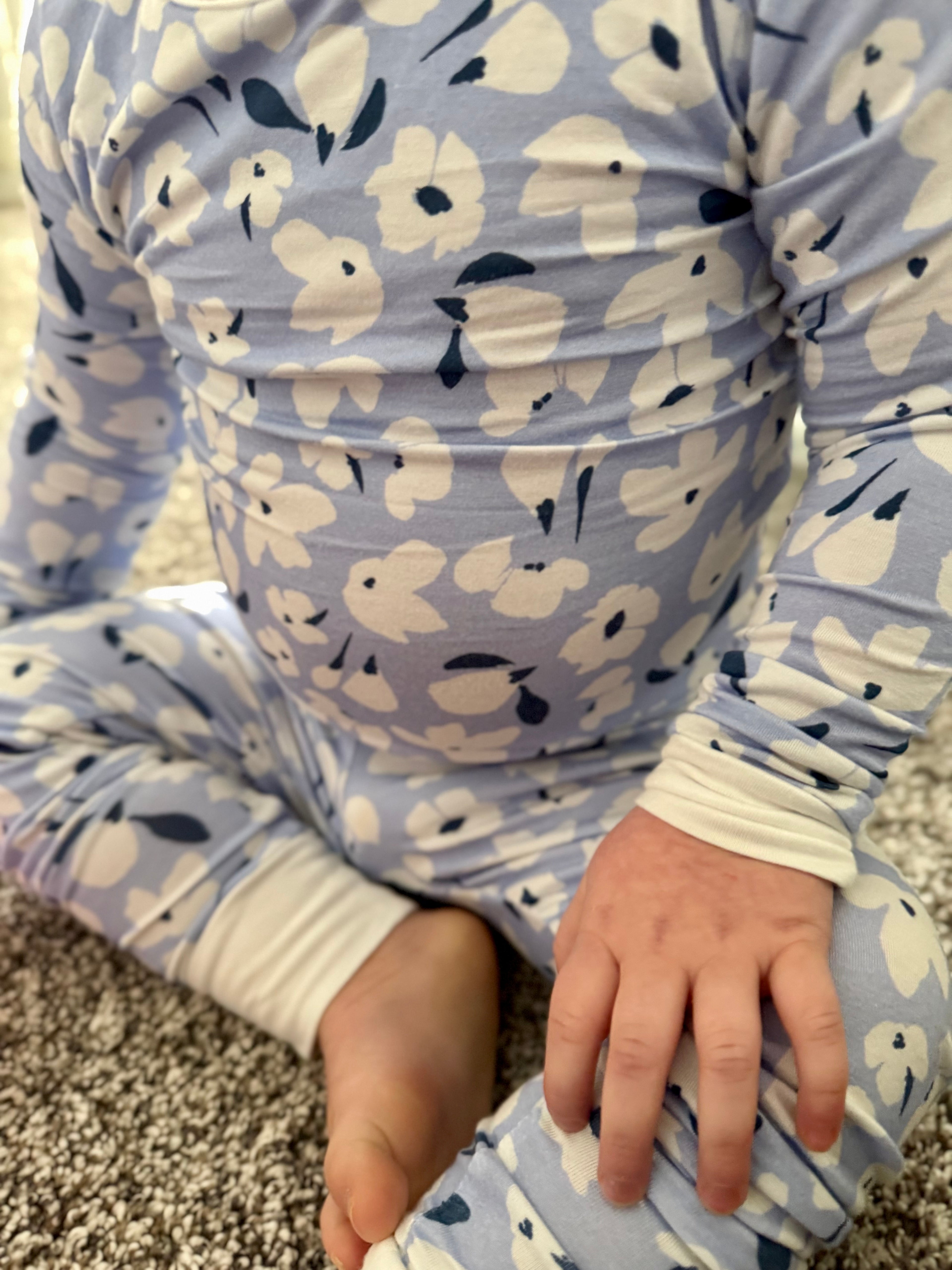 Child wearing a blue pajama with white floral print sitting on a carpeted floor.