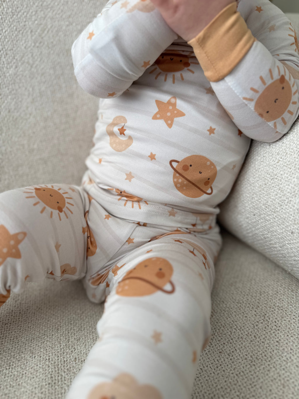 Baby In off white bamboo baby pajama with space, stars, sun and clouds in neutral colors. 