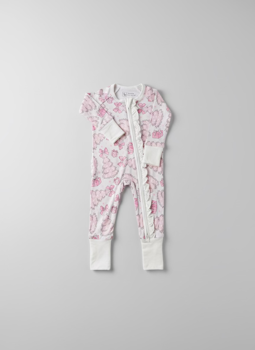 Toddler wearing bamboo baby pajama. Baby Bamboo convertible footie pajama that is pale pink with pink and white christmas trees, bows, presents and stars. Pajamas are super soft, great for sensitive skin and will grow with your little - the mittens and feet are adjustable!