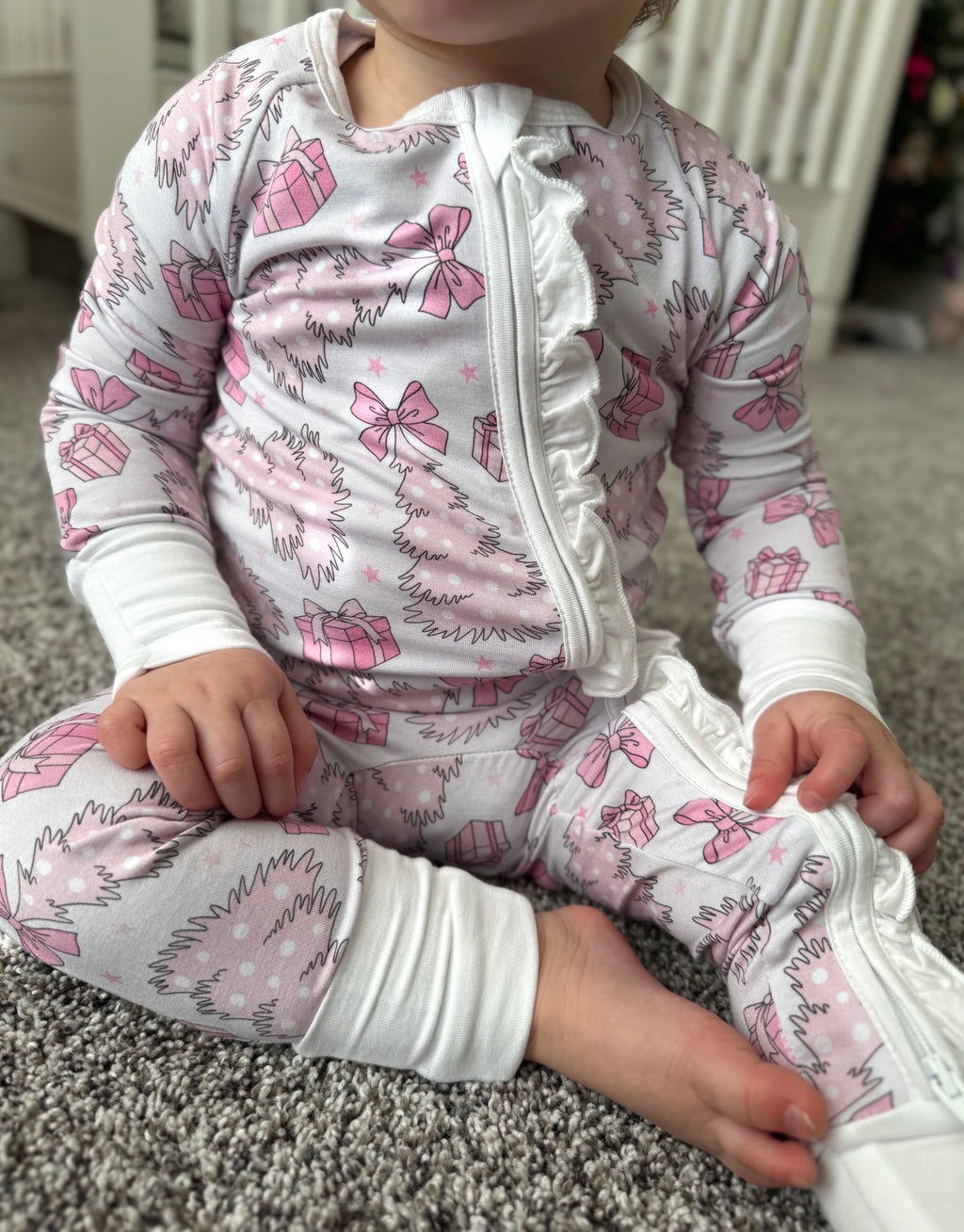 infant wearing convertible soft bamboo pajamas with ruffle zipper. Baby Bamboo convertible footie pajama that is pale pink with pink and white christmas trees, bows, presents and stars. Pajamas are super soft, great for sensitive skin and will grow with your little - the mittens and feet are adjustable!