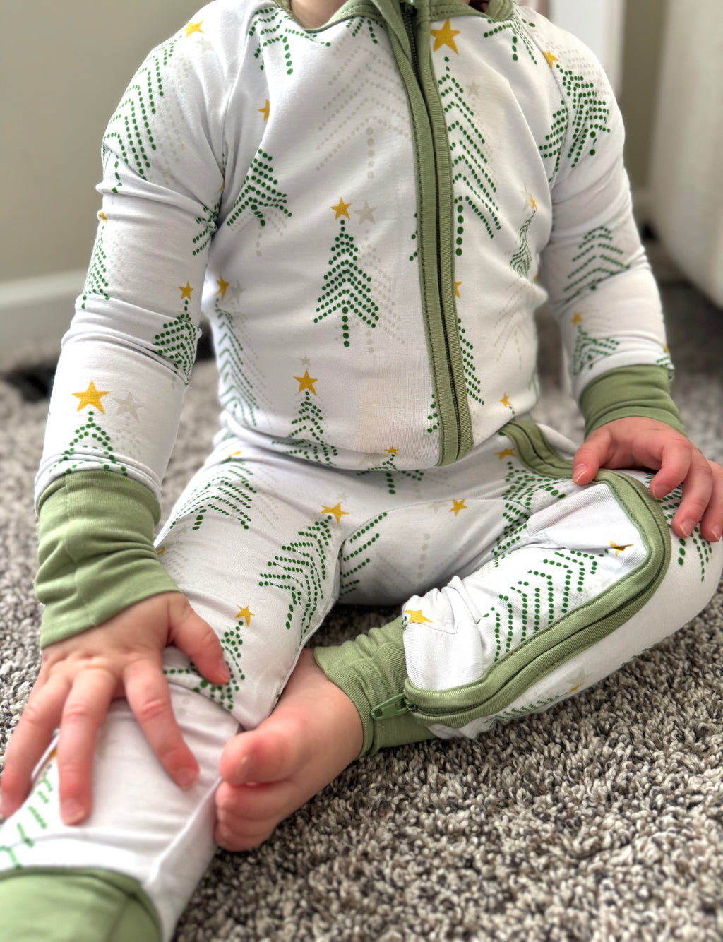 Infant wearing Christmas Bamboo Pajama white background with pine trees in light green and grey and stars. Bamboo pajamas are super soft, durable and adorable. The convertible footie pajamas have adjustable feet and mittens to grow with your little. 