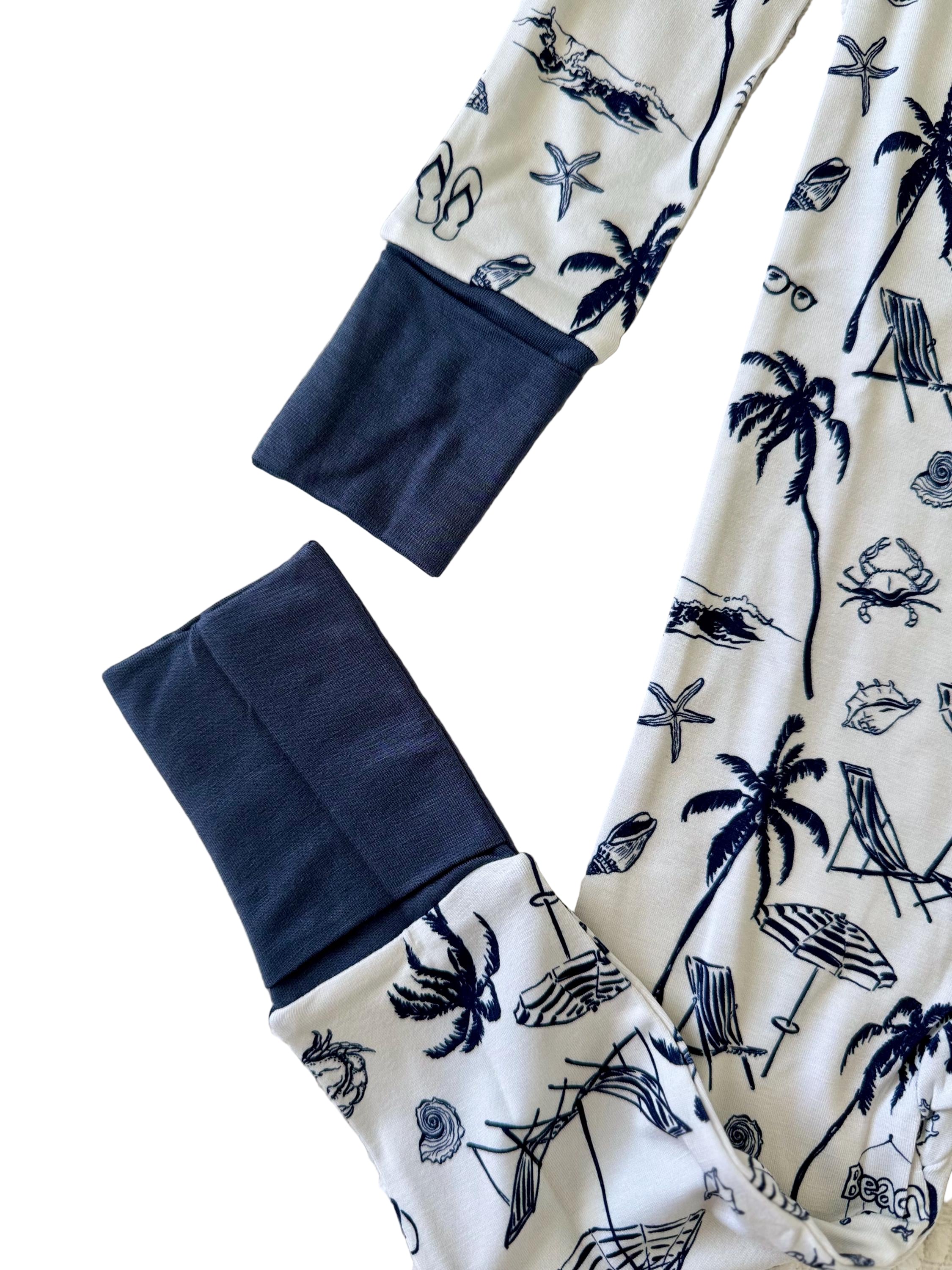 Little Mallard designed pajama with white background with blue palm tree, shells, waves, umbrella, chair, crab, sunglasses and beach theme with convertible mittens and feet. 