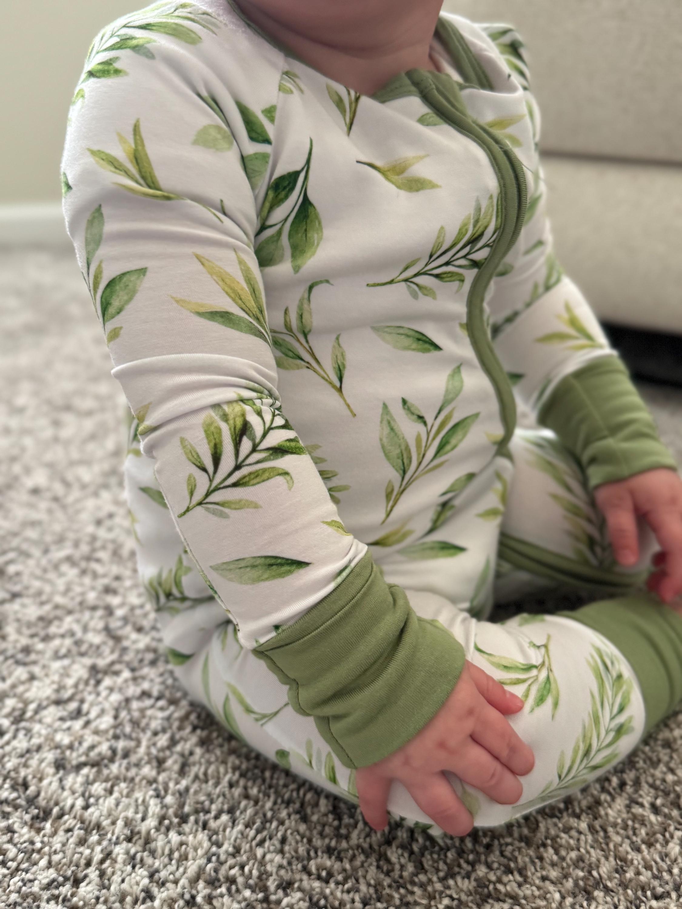 Baby wearing a green and white leaf-patterned outfit sitting on a carpeted floor.