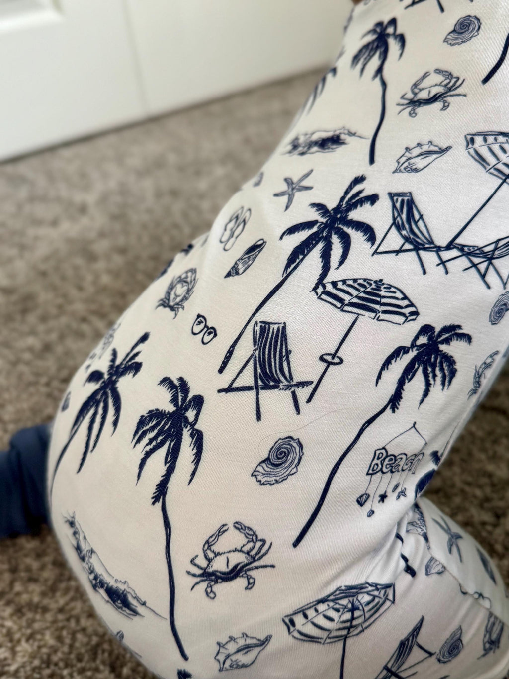 White bamboo baby pajama with blue beach-themed pattern on a carpeted floor.